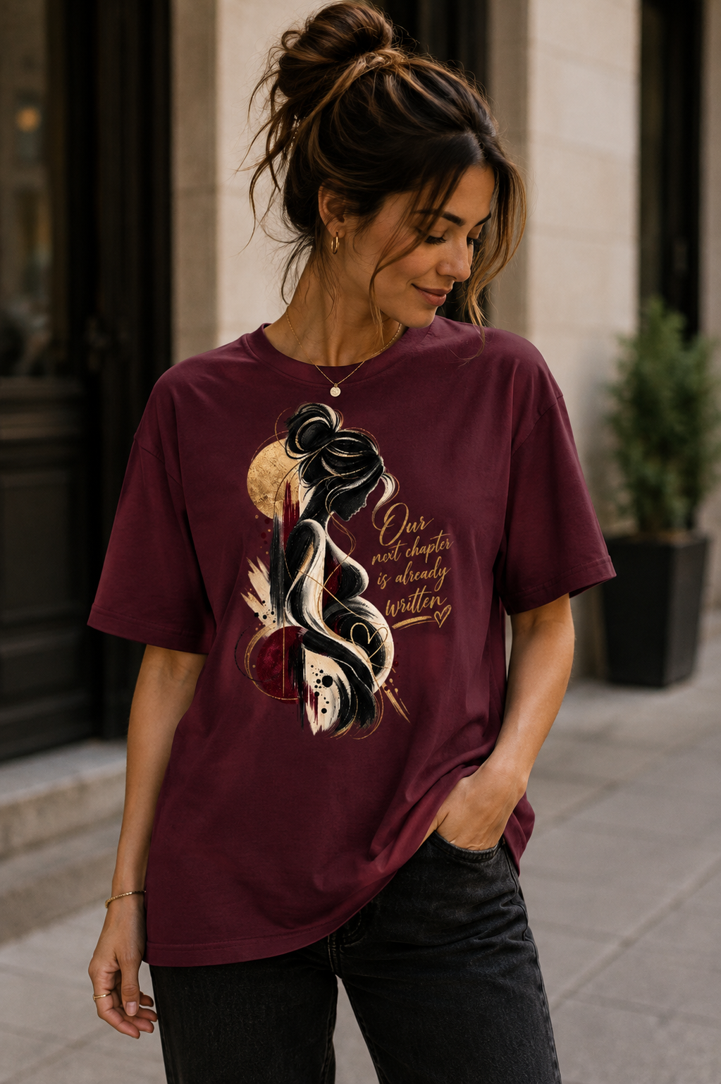 Burgundy women’s pregnancy announcement graphic T-shirt featuring an artistic expectant mother silhouette in black and gold with the message Our next chapter is already written.